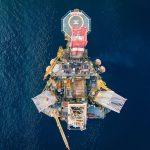 Vista aérea de uma plataforma de petróleo offshore com heliponto em meio ao oceano.