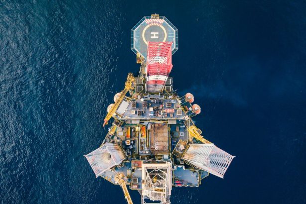 Vista aérea de uma plataforma de petróleo offshore com heliponto em meio ao oceano.