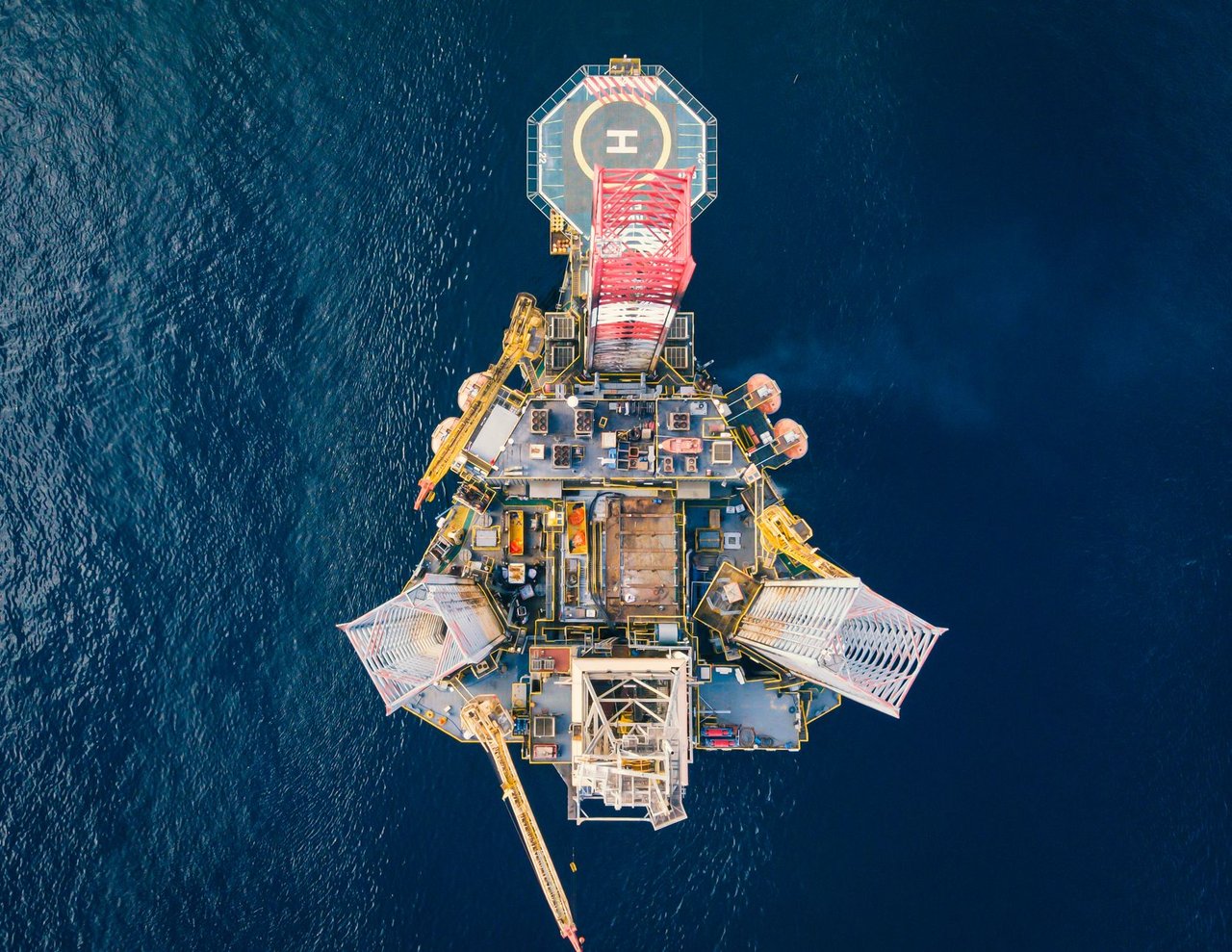 Vista aérea de uma plataforma de petróleo offshore com heliponto em meio ao oceano.