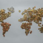 Mapa-múndi formado por moedas sobre um fundo cinza, simbolizando a economia e as finanças globais.