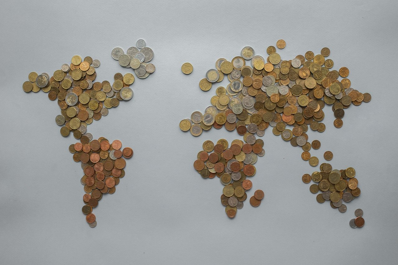 Mapa-múndi formado por moedas sobre um fundo cinza, simbolizando a economia e as finanças globais.