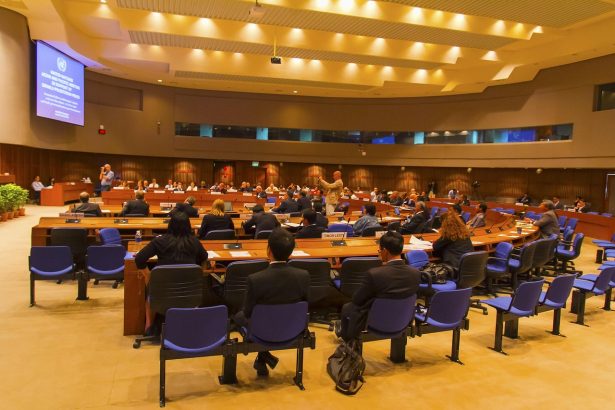 Sala preparada para uma reunião ou conferência institucional, com mesas e cadeiras organizadas.